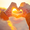Gloved hands in a heart shape against a backdrop of a sunrise