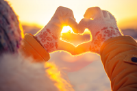 Gloved hands in a heart shape against a backdrop of a sunrise