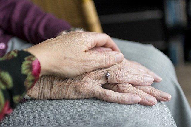 The hand of a middle aged person is on top of the hands of an elderly person.