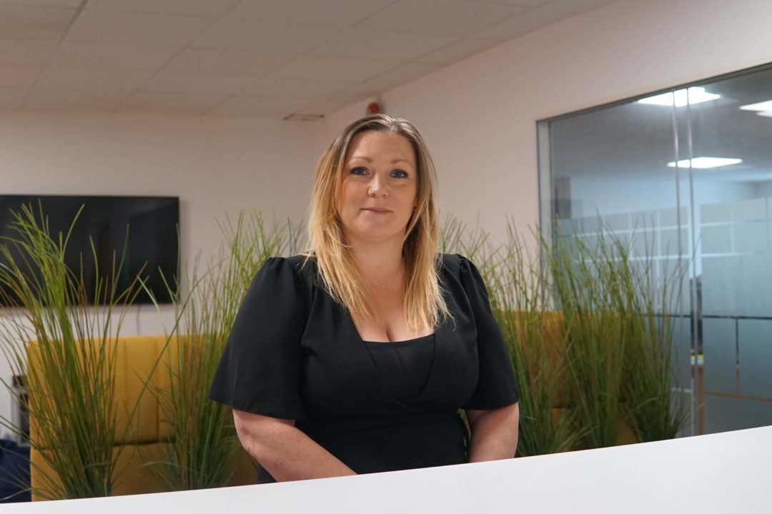 A blonde haired woman is wearing a black top and sat at a table. The woman is Amy-Jayne Carr, a Regional Manager of ND Care & Support, which is growing its private care division.