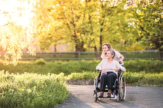 Carer and wheel chair assisted client going for a stroll in the park